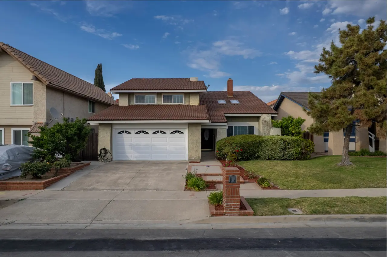 Front of the two-story home with a tile roof, a two-car garage, and a front lawn