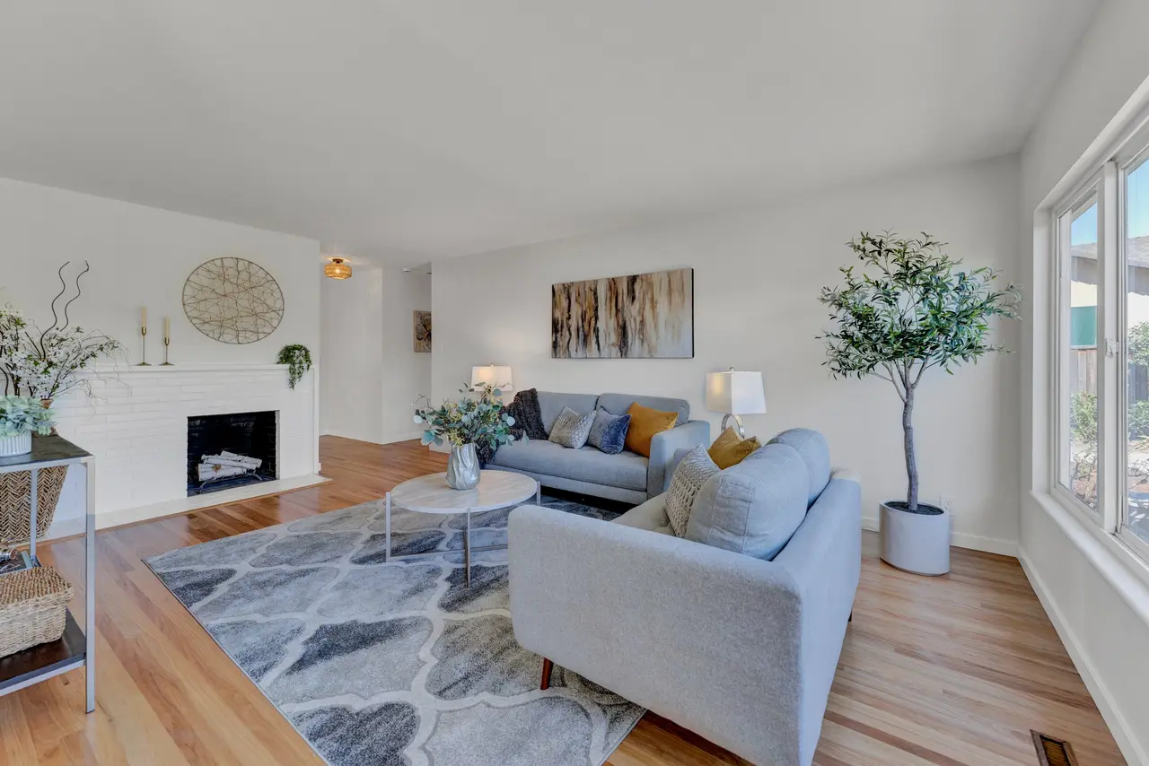 Living room with hardwood floors, a white brick fireplace, and large windows