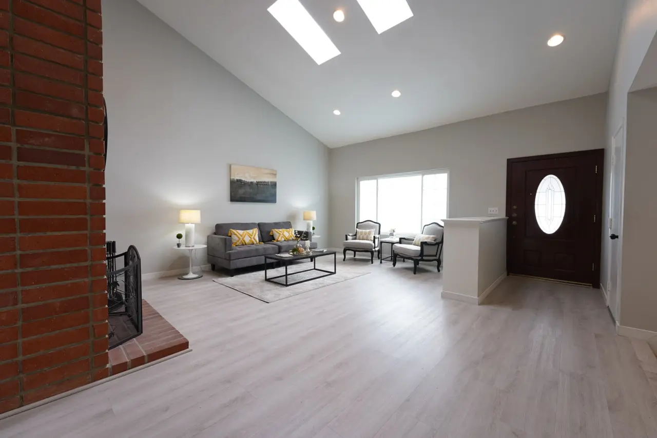 Living room with a vaulted ceiling, skylights, and a brick fireplace