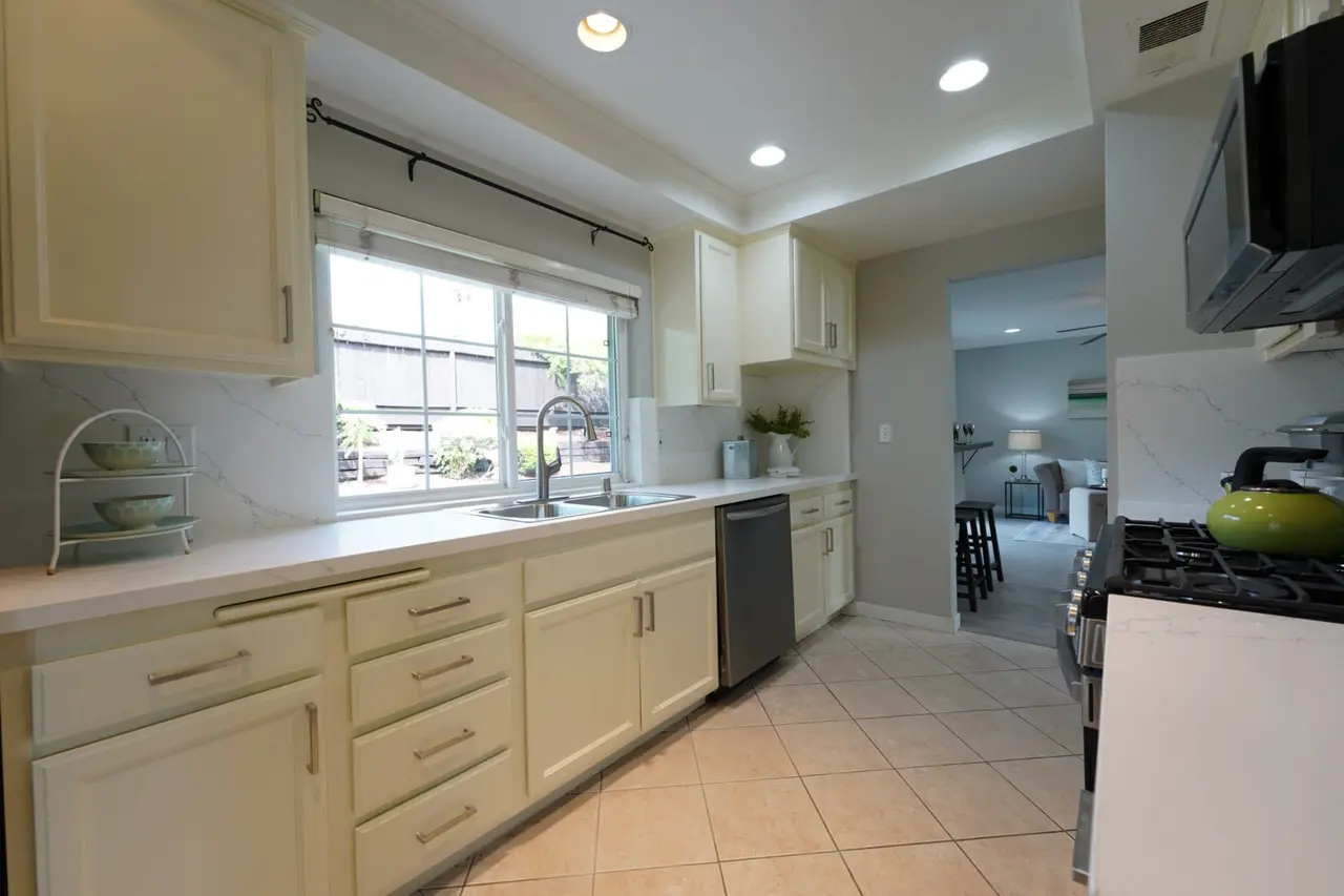 Kitchen sink under a window with white counters and a dishwasher