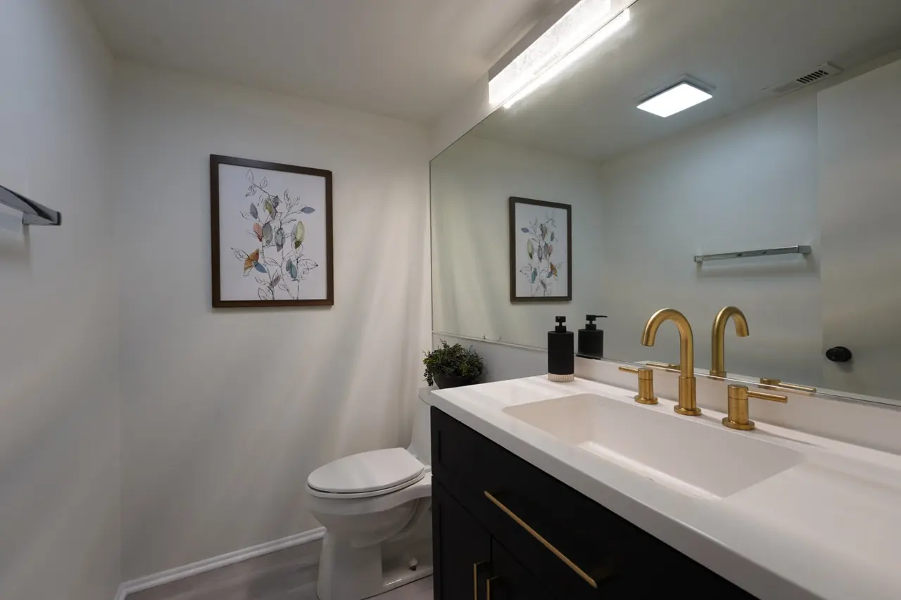 Bathroom with a dark vanity, a white counter, and gold faucets